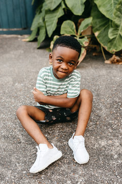 An adorable, stylish little boy sitting outside on the concrete.