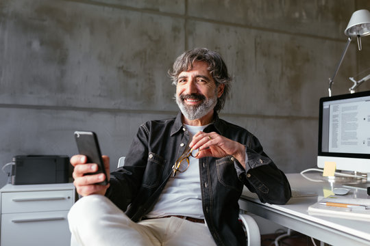 Cheerful mature man browsing smartphone in office