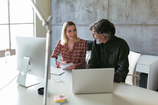 Cheerful trainee writing after mature mentor in office