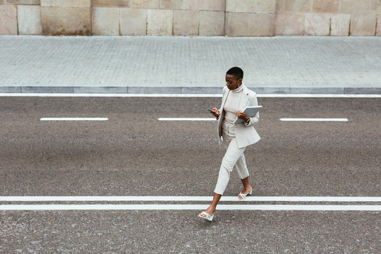 African American manager using smartphone and crossing road