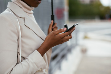 Crop black female using smartphone under umbrella