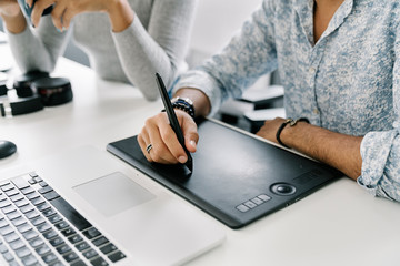 Close up of a curly haired man working with a graphic tablet while curly haired woman is helping him.