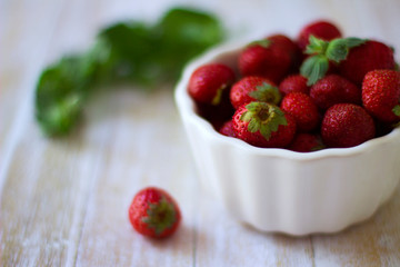 Ripe red strawberries in a white bowl on a light wooden background. Delicious and healthy food. Healthy organic products concept. Harvesting.