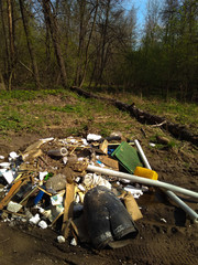 A huge mountain of household waste lies on the road in a green, blooming forest.