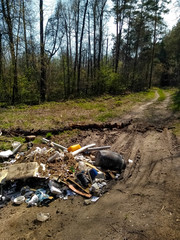 A huge mountain of household waste lies on the road in a green, blooming forest.