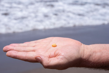 Fototapeta na wymiar Small sea shell in a human man hand - beach and waves on background