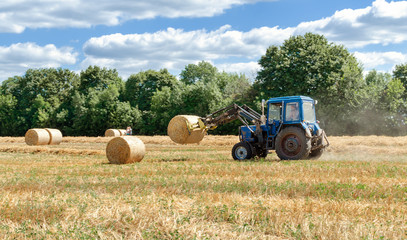 straw in round bales and a tractor in the field