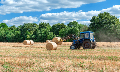 straw in round bales and a tractor in the field