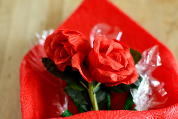 Fake roses in a red paper bouquet over a wooden table