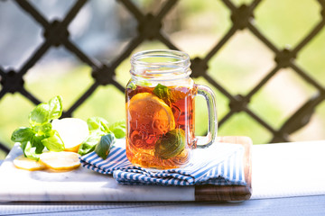 The glass of iced tea on wooden table. Cuba Libre or long island cocktail, cold drink or lemonade with lemon and basil. Balcony on back yard