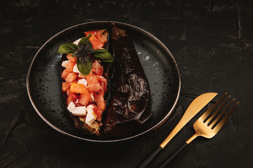Baked eggplant with tomato salad, feta cheese and basil on a black plate