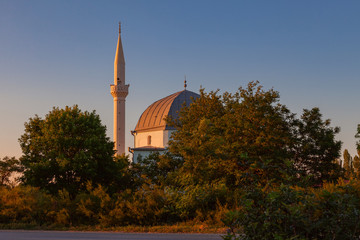 White mosque with a high minaret illuminated by the rays of the setting sun