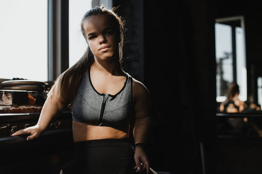 Portrait of a young dwarf woman in a sport bra. Shi is looking at the camera.