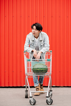 Thoughtful Asian Man standing with Cart against Red Background