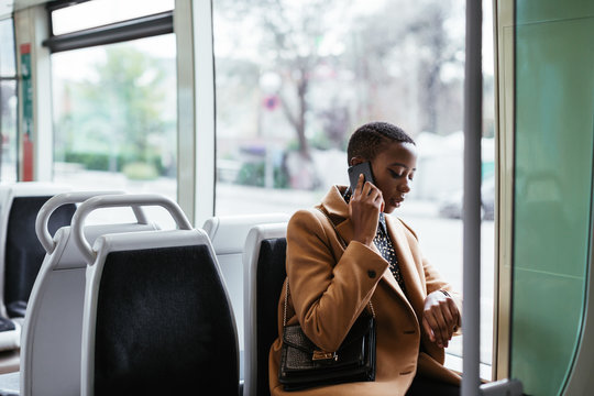 African American woman speaking on phone and checking time in modern transport
