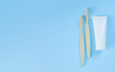 Eco-friendly bamboo toothbrushes next to toothpaste on light blue background. Top view with space for your text