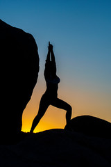 Woman doing yoga in the sunset with yellow and blue sky