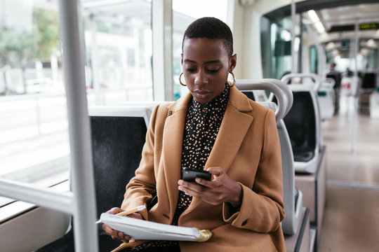 Black woman with notebook using smartphone in contemporary vehicle