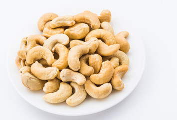 fresh cashew nuts on a white dish above the white background