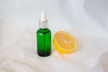 Bottle of lemon essential oil with lemons on white fabric background. Beauty cosmetic natural skincare product mock up.