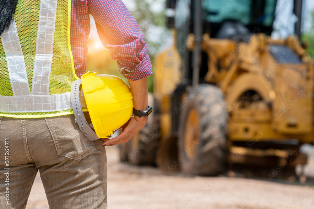 Wall mural engineer woman holding yellow helmet for workers security on background of construction car vehicle 