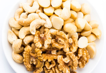 Variety of fresh nuts on a white dish above the white background