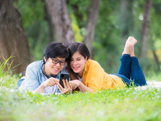 Asian LGBT couples relax in the park while listening to music on their mobile phones