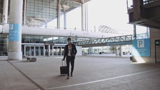 Traveler in Business Suit Walking in Airport with His Luggage and Wearing Mask