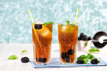 The glass of iced tea with blackberry on wooden table. Cuba Libre or long island cocktail, cold drink or lemonade with lemon and basil. Green turquoise on background