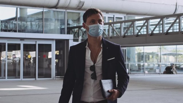Young Male Traveler with Surgical Mask Walking Towards Camera in Airport