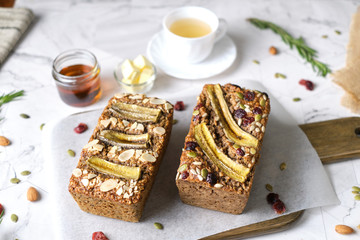 Loaf of Vegan Oatmeal Banana Bread topped with nut, seed, almond slide and banana set on cafe table.