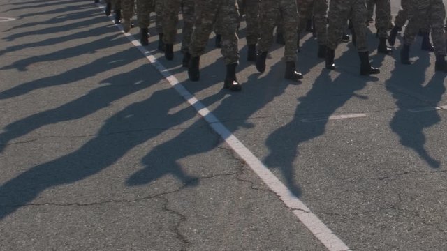 Soldiers marching down city streets, wearing camouflage uniforms. Low angle view of their legs and feet as the march by.