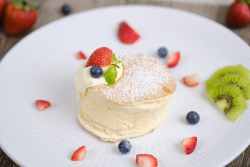 Fluffy souffle pancakes with cream and berries on white plate set on cafe table.