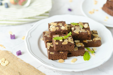 Fototapeta na wymiar Squares Chocolate brownie with almond sliced set on white cafe table.