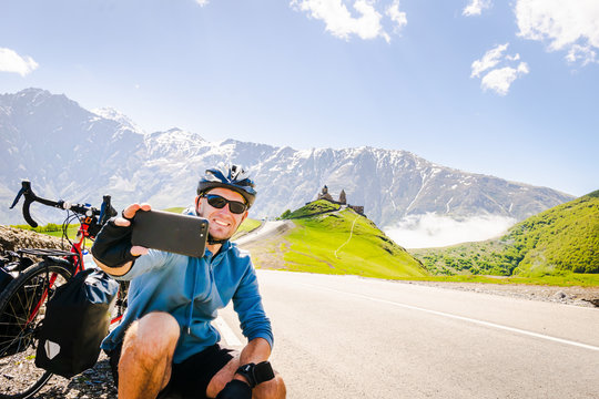 Male person takes a selfie on bicycle vacation in scenic caucasus mountain region. Travel in Kazbegi.