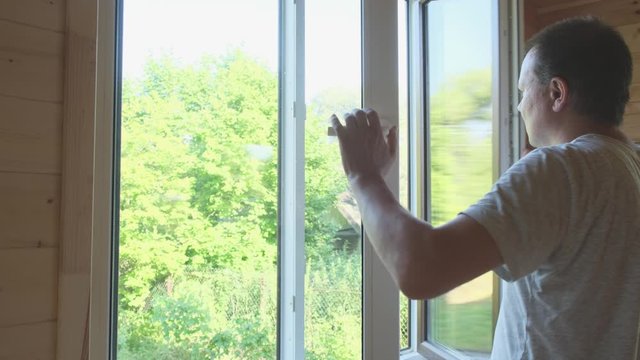 A man closes a white plastic window by the handle.