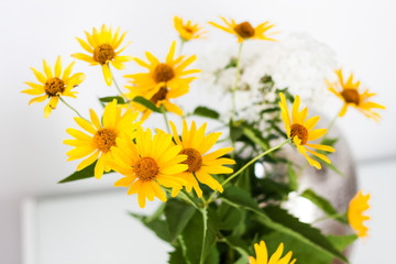 bouquet of yellow flowers in a vase on a white table in the room.