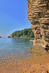 Girl standing on rocks in swimsuit on the beach Mogren Budva in Montenegro and sunbathe. Tourism in Europe and beach vacations. Cove, bay, rocky mountains , sand pebbles and pure water to swim, bathe