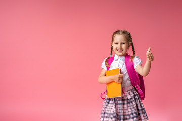 little girl with a backpack and a book gives a thumbs-up sign of approval. - Powered by Adobe