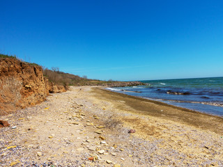 Deep sandy cliff on the background of blue sky. The destruction of the coast as a consequence of soil erosion. Landslide - threat to life.