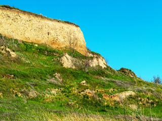 Deep sandy cliff on the background of blue sky. The destruction of the coast as a consequence of soil erosion. Landslide - threat to life.