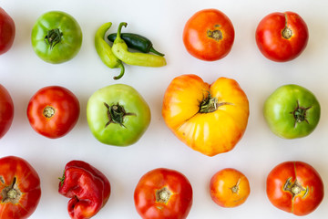 Rows and columns of red and green tomatoes on white background with one of the spaces replaced by peppers.