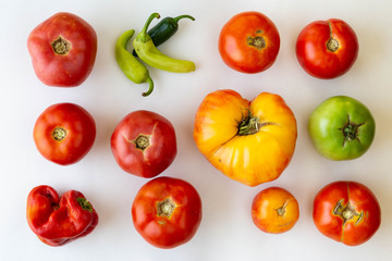 Rows and columns of red and green tomatoes on white background with one of the spaces replaced by peppers.