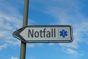 A shield or sign showing a emergency room, ER, in German language on the background of blue sky and cirrus clouds