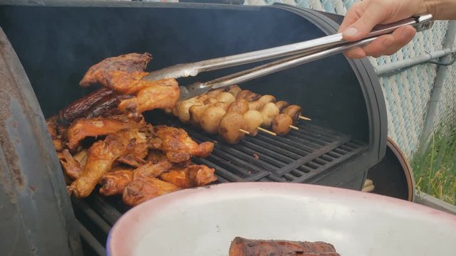 Home cooking - Transferring cooked food like sausage and chicken wings from grill to bowl using tongs. Food has been previously barbecued and then placed in wood smoker for extra smoky flavor.