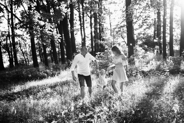 Lovely parents play with little daughter, smiling, caring dad and loving mom lift in air adorable baby girl, young family walking at the park, weekend outdoors, parenthood concept