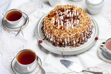 white layered almond cake with melted chocolate on top on a white tablecloth with a china set, vintage forks, almond flakes