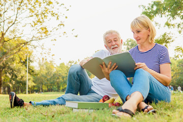 Happy Mature couple reading the book 
 together and having picnic in the garden at the summer day. Retirement, Picnic, Relax, Older, Lover and dating concept. 