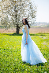 Fototapeta na wymiar Portrait of a girl in a light summer blue long dress adorned in her hair against a blossoming tree.