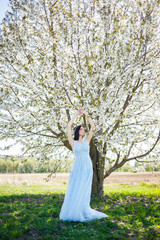 Young woman with beautiful make-up with a vintage hoop in a blue light dress with a bouquet posing on a background of green foliage in a park. Fresh portrait attractive girl with white flowers.